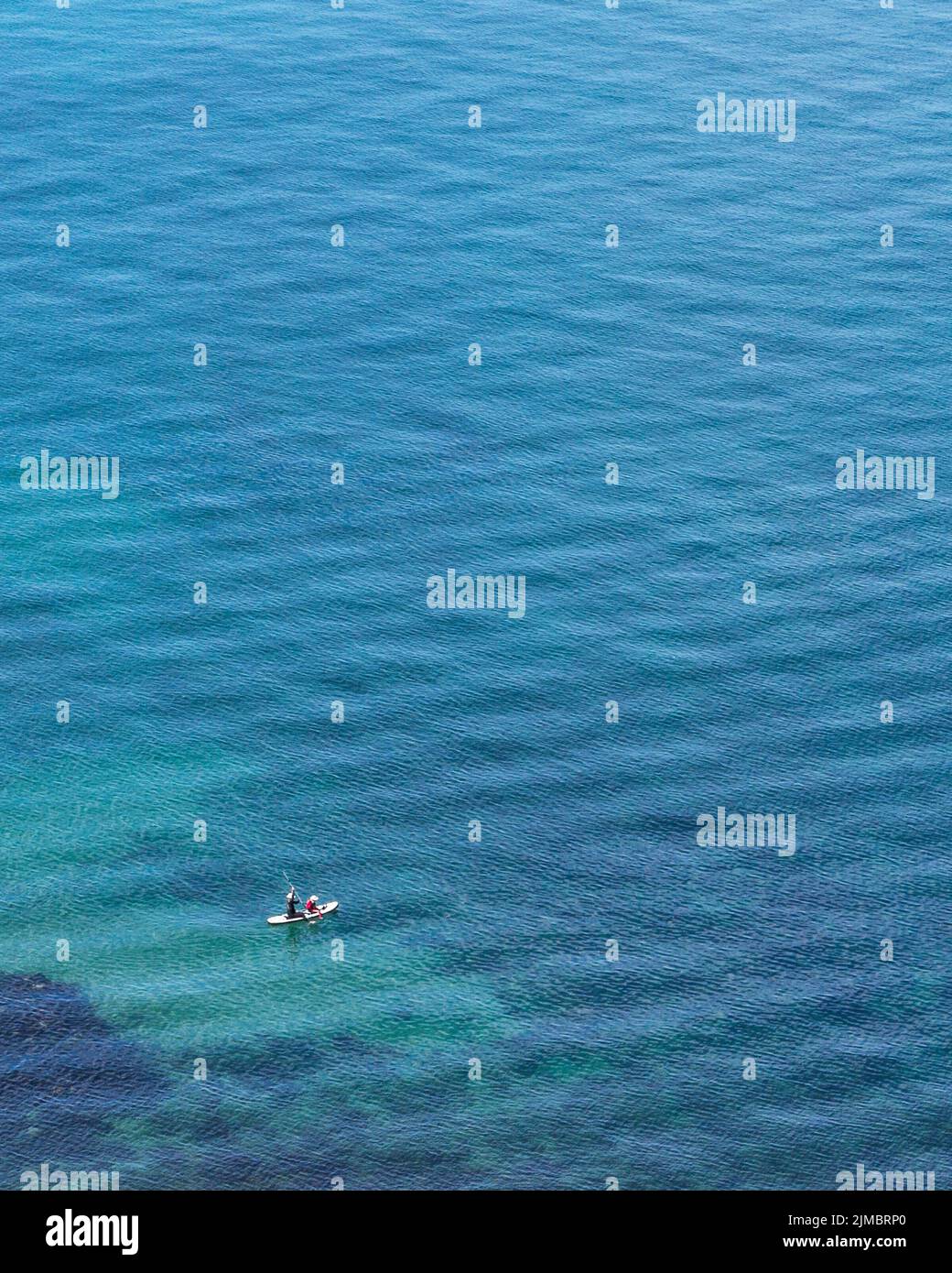 A couple paddle boarding off the coast look minuscule against the vastness of the sea. Health, fitness, holiday, vacation, adventure concept. Stock Photo