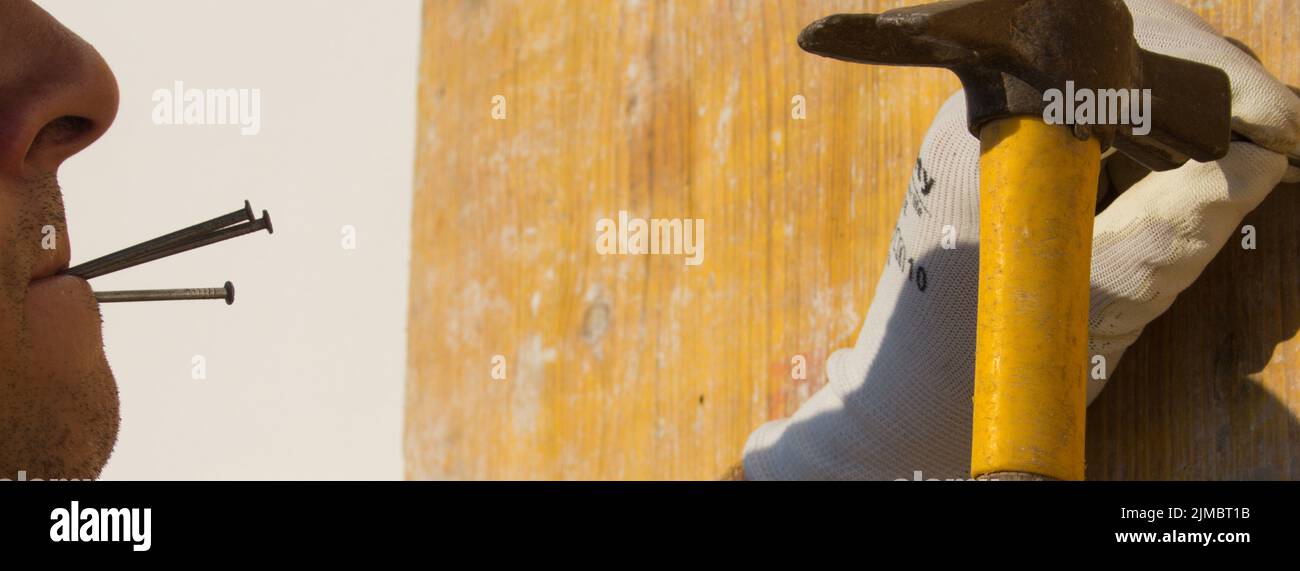 Image of a carpenter's mouth holding nails between his lips while