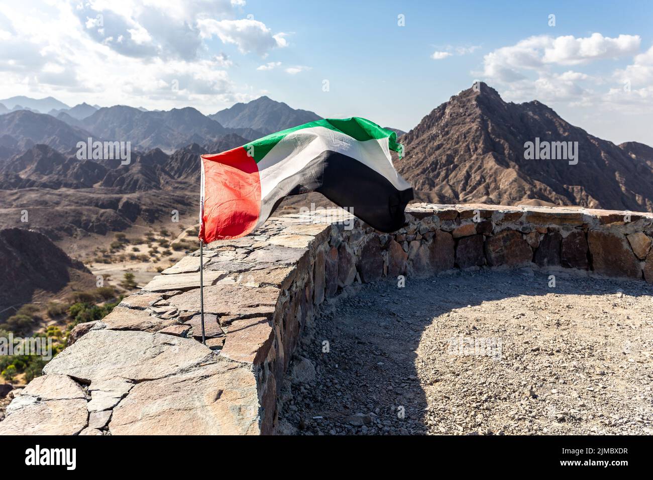 United Arab Emirates national flag waving on the wind, attached to a stone wall at the top od Wadi Shawka staircase, with Al Hajar Mountains. Stock Photo