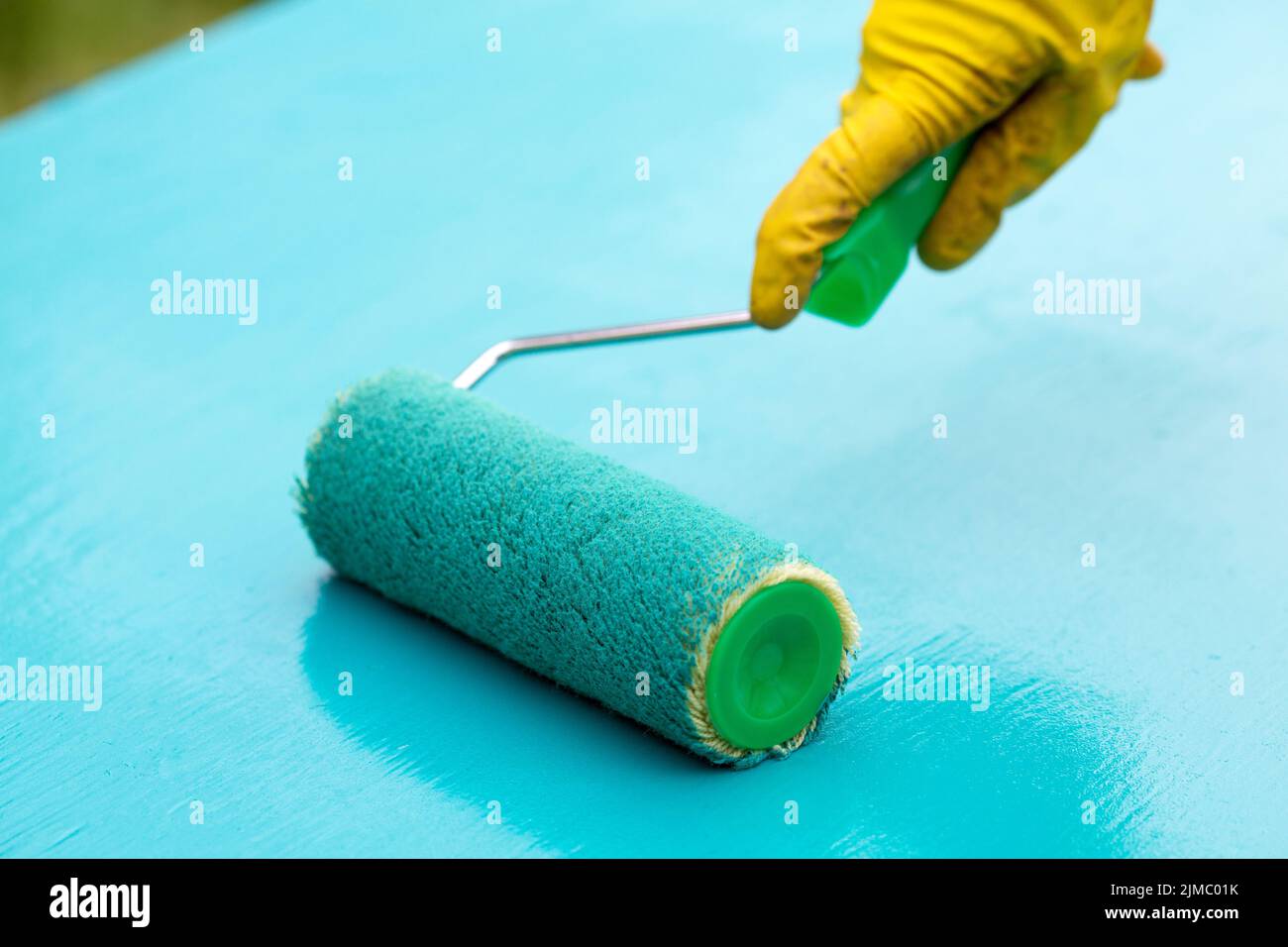 Paint roller in hand and board with turquoise paint Stock Photo