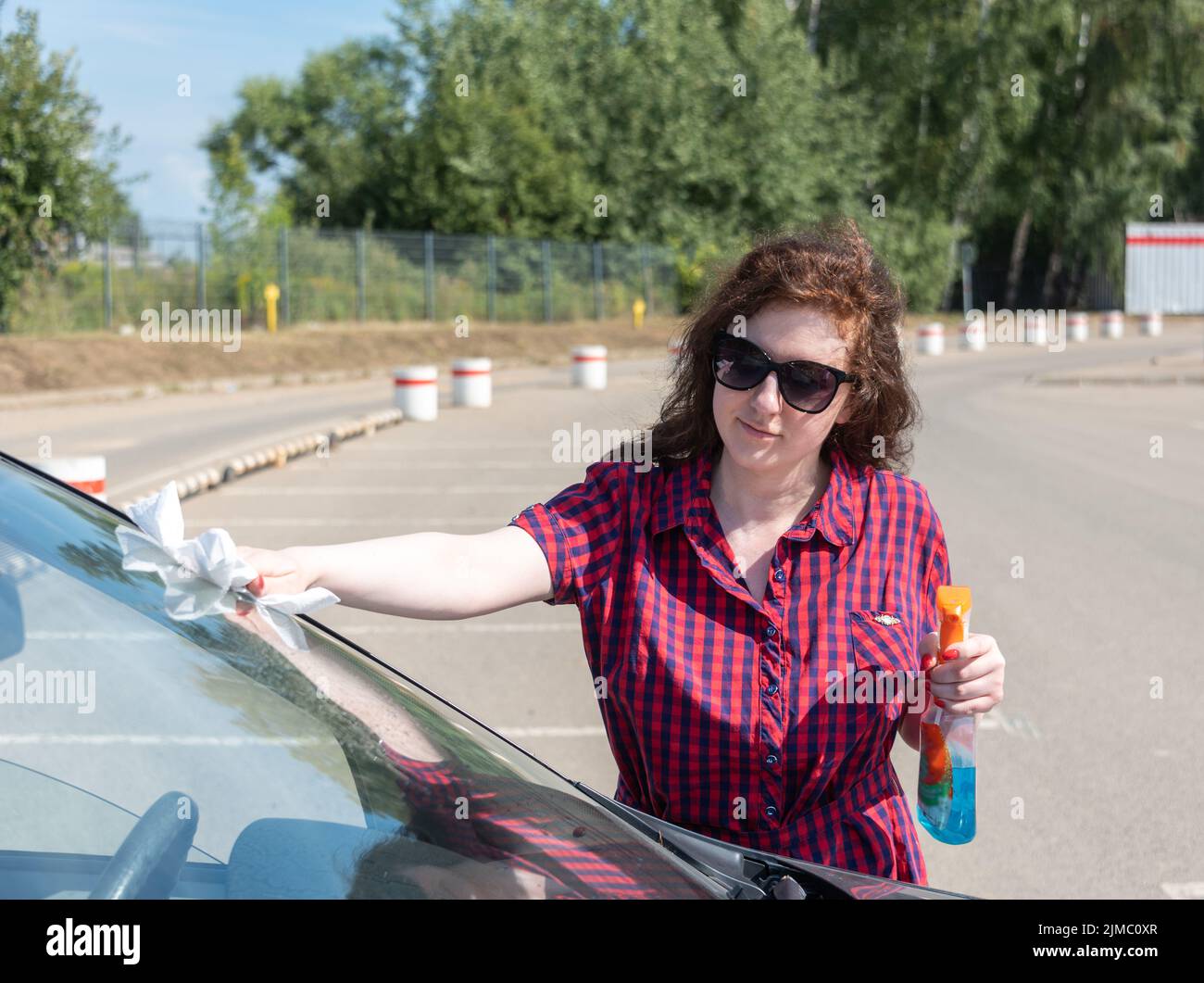 Young woman is wiping the windshield with a paper towel after spraying