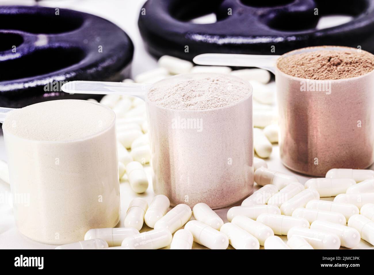 Measuring spoons of dietary supplement, various flavored whey and creatine pills, with weights in the background Stock Photo
