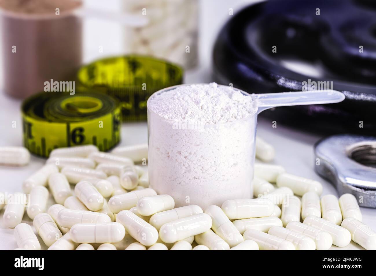 Measuring spoons of dietary supplement, various flavored whey and creatine pills, with weights in the background Stock Photo