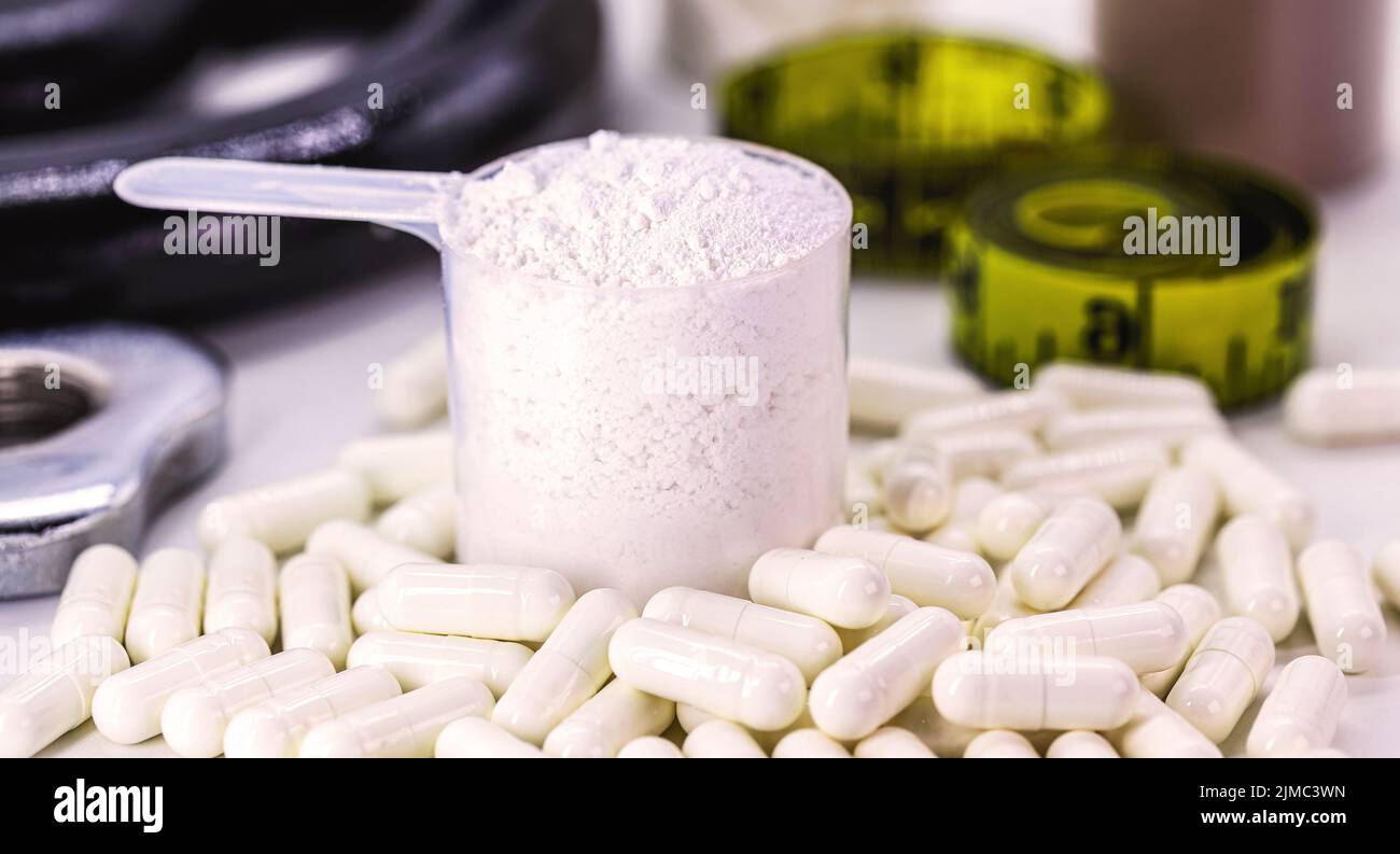 Creatine, food supplement to strengthen muscle fibers, with weight for bodybuilding in the background. White background with copyspace Stock Photo