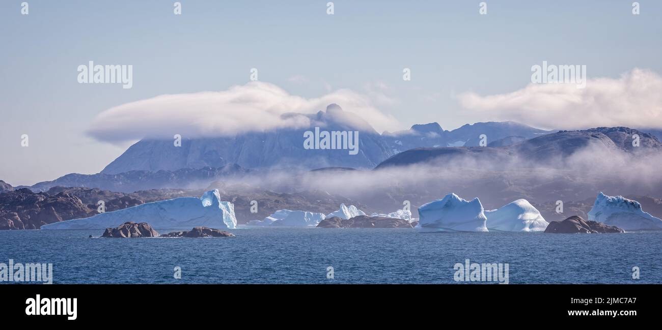 Panorama of icebergs in Prince Christian Sound against backdrop of mountains with low hanging cloud in Greenland Stock Photo