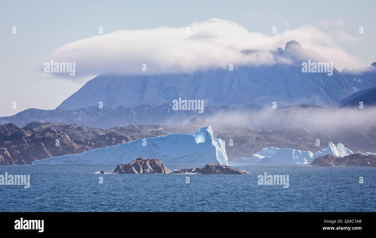 Panorama of icebergs in Prince Christian Sound against backdrop of mountains with low hanging cloud in Greenland Stock Photo