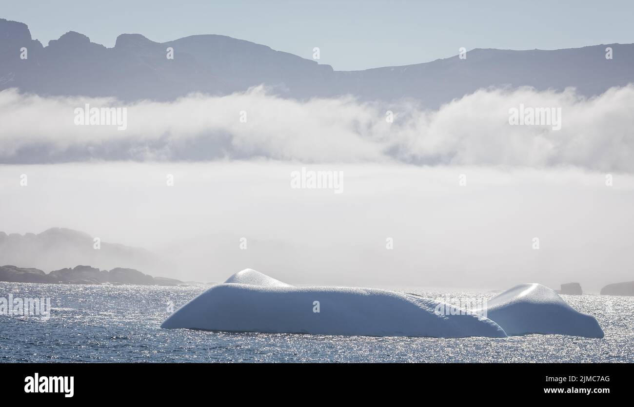 Iceberg in Prince Christian Sound with mountains and low hanging cloud in background in South Greenland Stock Photo