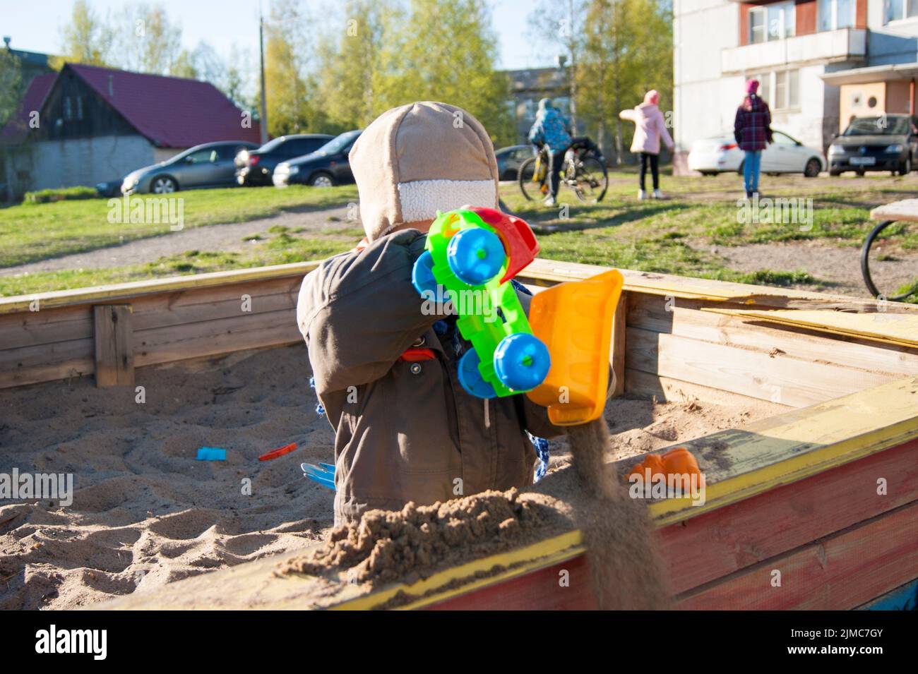 A little boy of three years old is playing on a cool spring sunny day in the sandbox in the city yard with his toy truck Stock Photo