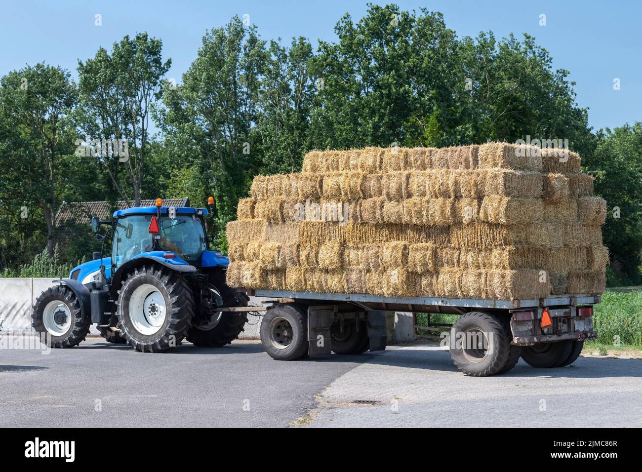 Blue tractor with plain old farm wagon with straw bales stacked Stock Photo