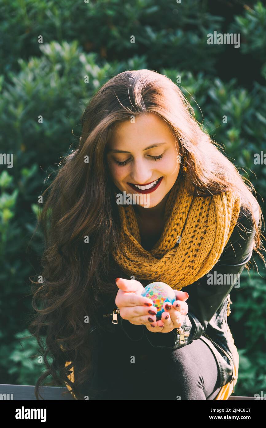 Attractive stylish woman holding a small world globe in her cupped hands as she enjoys the sunshine in a park in autumn smiling as she imagines her ne Stock Photo