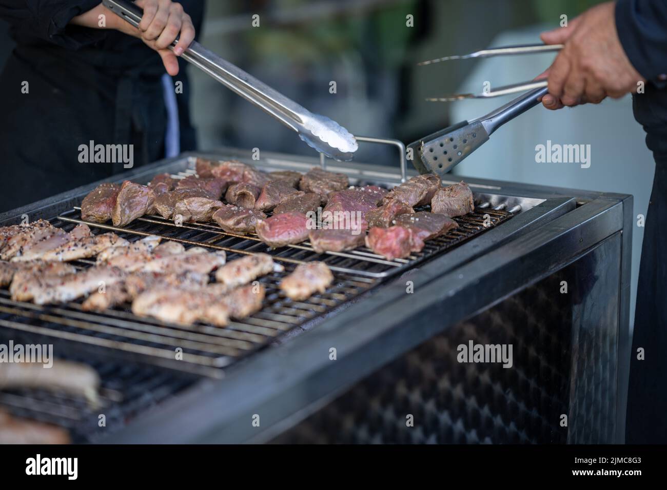 Food, Deutschland, Rheinland-Pfalz, July 30. Rohes Fleisch liegt auf einem Grill und wird mit Grillzangen gewendet. Stock Photo