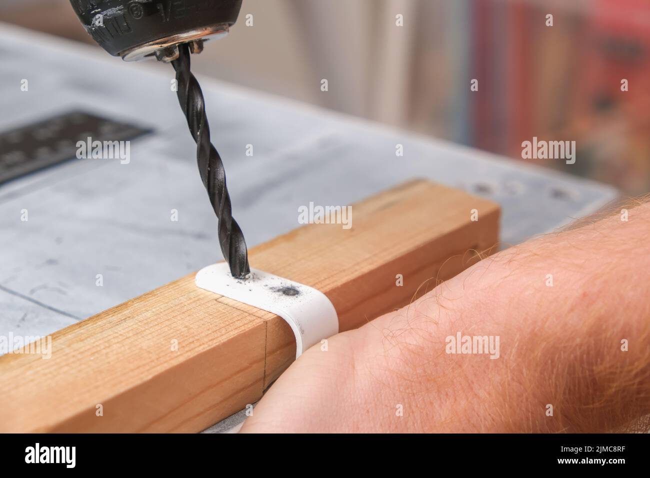 A man drills holes in an iron hook with a drill to hang a wooden screen