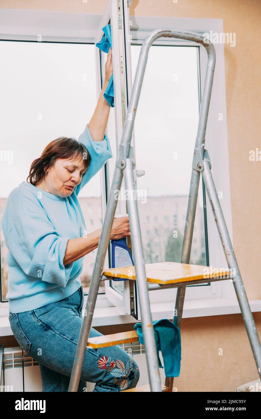 Happy Shy Mature Woman Cleaning Window. Caucasian Woman Middle Age. Elderly Woman Cleaning Apartment. Active Seniors Concept. Housewife. Concept Of Stock Photo