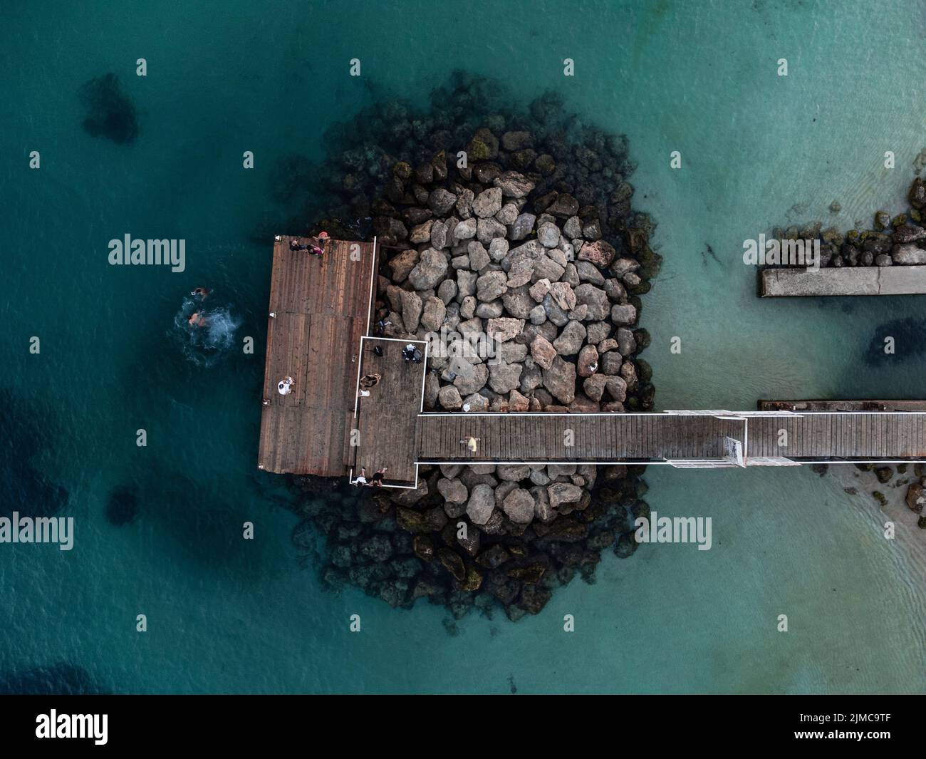 An aerial view of a jetty on rocks in the clear turquoise water of ...