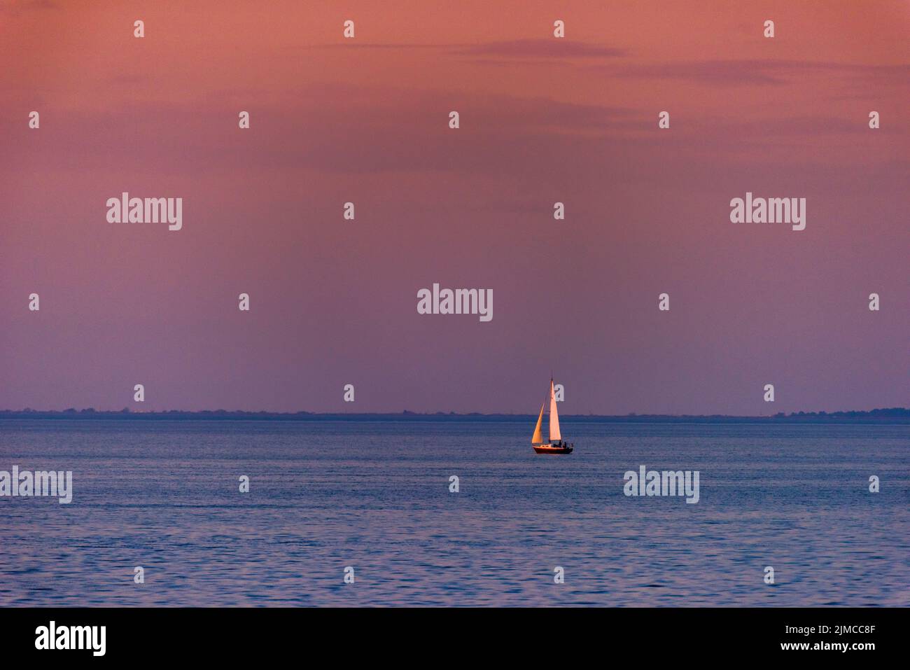 A singe sailboat floats on Mobile Bay at sunset. Stock Photo