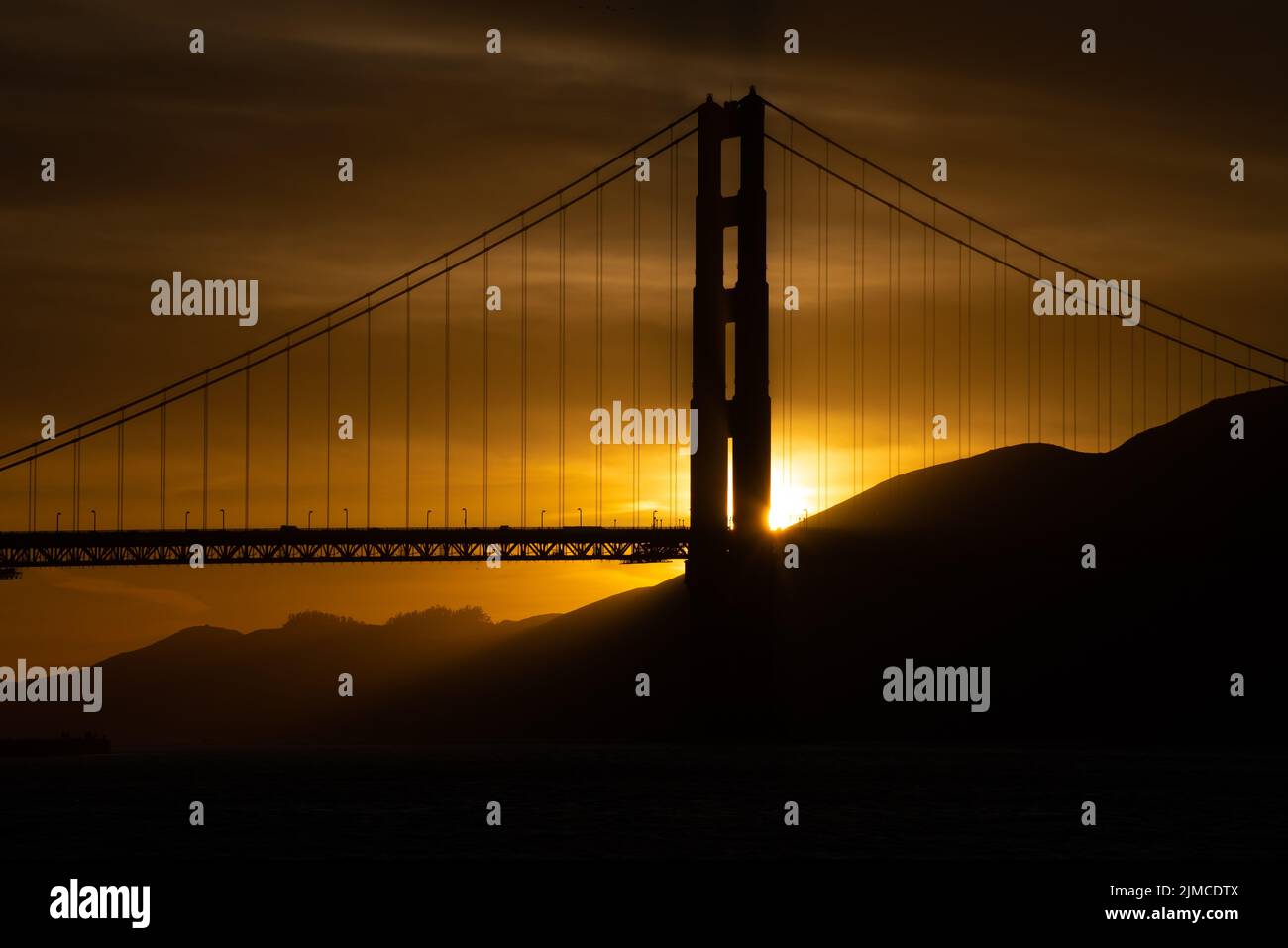 Sunset behind the Golden Gate Bridge.  Bright golden yellow against the silhouette of the bridge Stock Photo