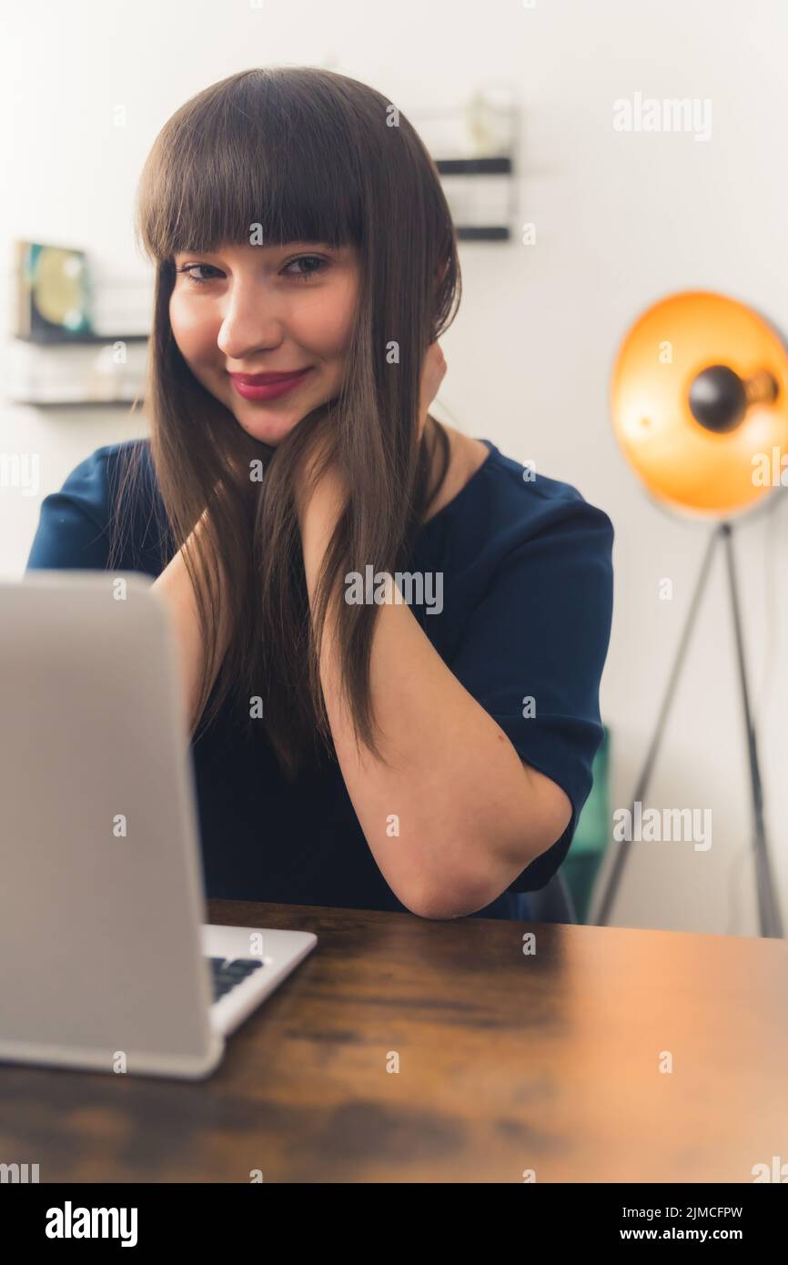 Attractive young brunette woman freelancer sitting at a table and enjoying working remotely using her laptop. High-quality photo Stock Photo