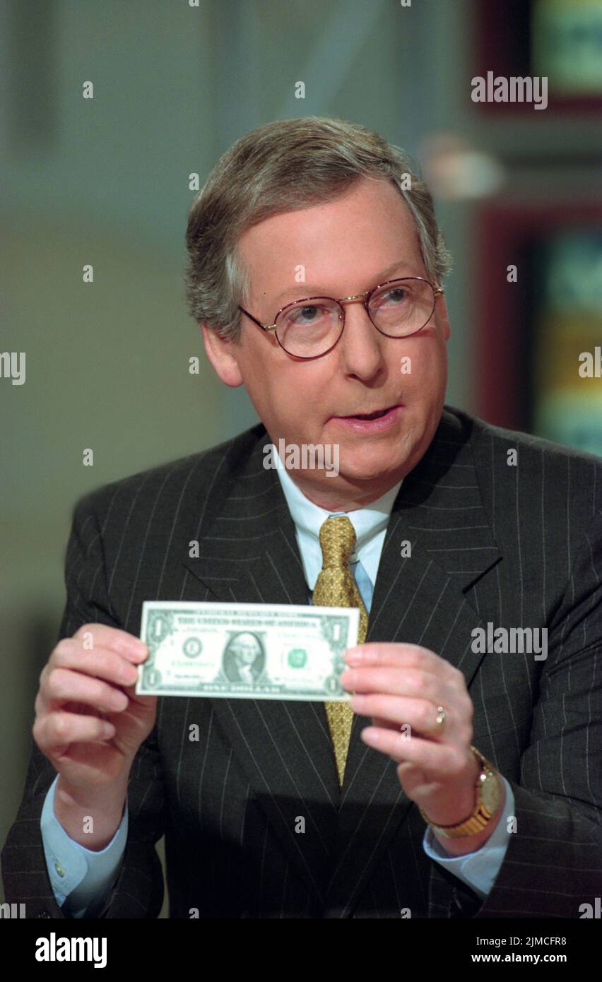 U.S. Senator Mitch McConnell holds a dollar bill to illustrate his point on the Republican tax cuts during NBC's Meet the Press, August 1, 1999 in Washington, D.C. Stock Photo