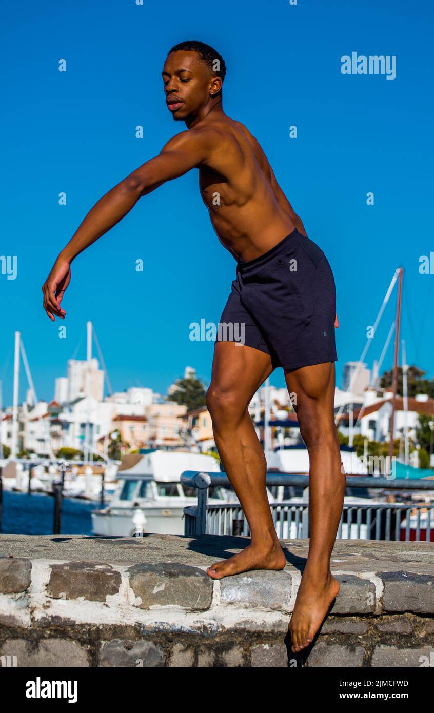 Ballet dancer with blue ocean water and sailboats behind him Stock Photo