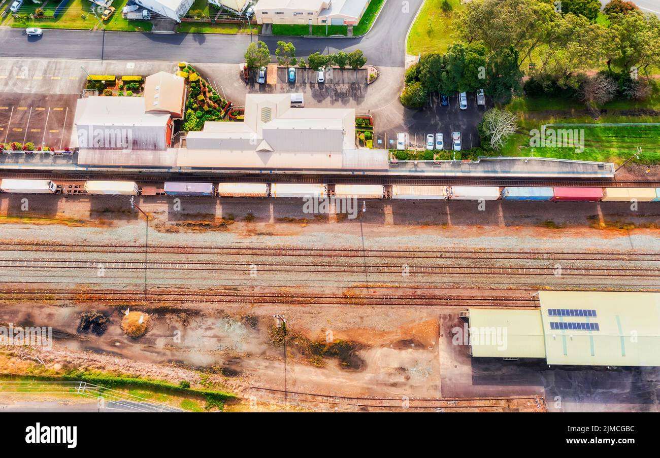 Local regional railway station in Taree town of Australia - aerial top down view over platforms, terminal, tracks and cargo train. Stock Photo
