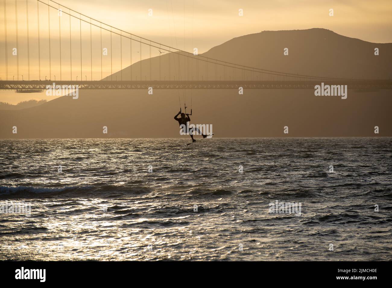 Kite surfer hanging in flight beneath the profile of the Golden Gate Bridge silhouetted against the backdrop of the Marin Headlands Stock Photo