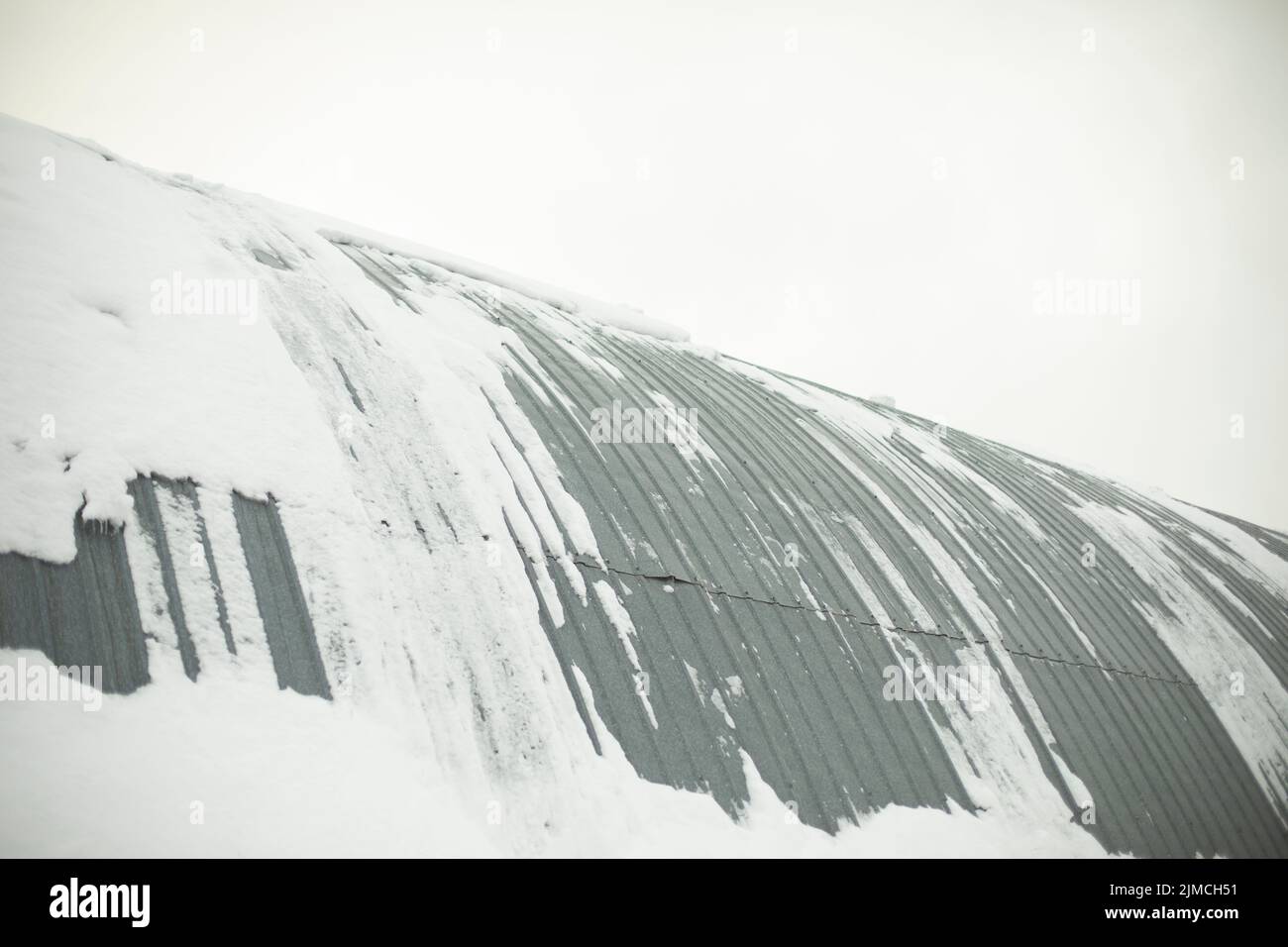 Warehouse building is in snow. Steel wall. Snow rolls down roof. Ribbed