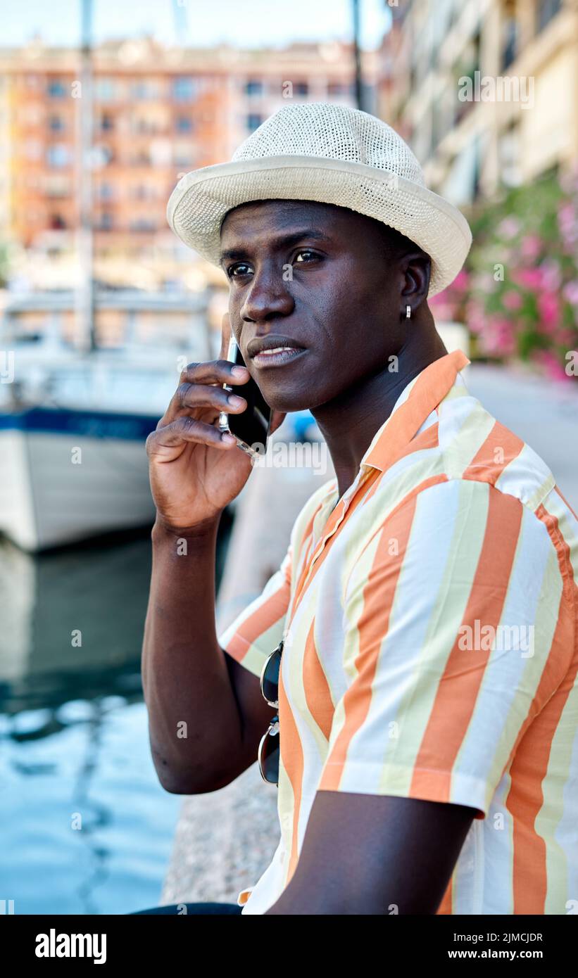 Side view of smiling African American businessman while having phone conversation on harbor near sea with boat Stock Photo