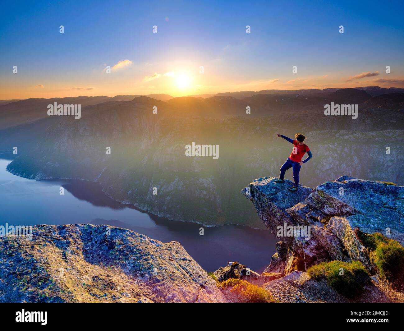 Woman standing on a rocky outcrop at Kjerag above the Lysefjord pointing her finger into the distance, sunset, Lyseboten, Rogaland, Norway Stock Photo