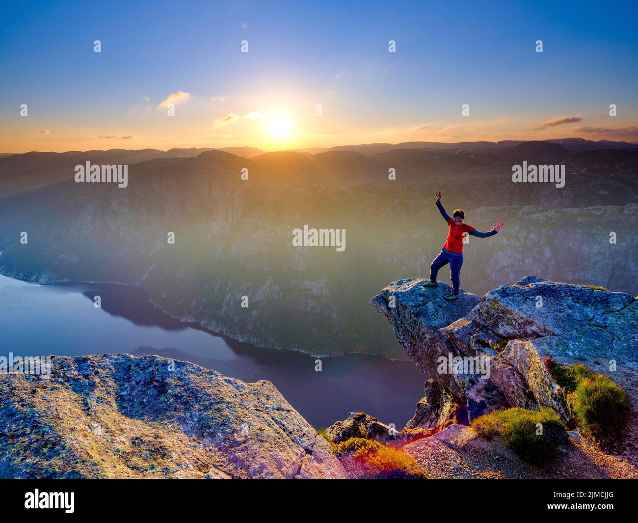Woman standing with spread arms on a rocky outcrop at Kjerag above the Lysefjord, sunset, Lyseboten, Rogaland, Norway Stock Photo