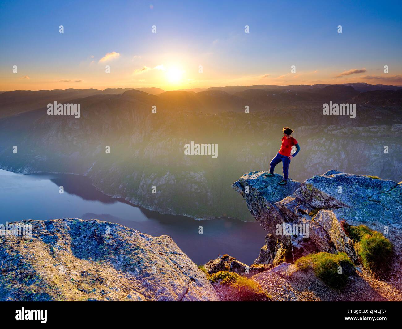 Woman standing on a rocky outcrop at Kjerag above the Lysefjord, sunset, Lyseboten, Rogaland, Norway Stock Photo