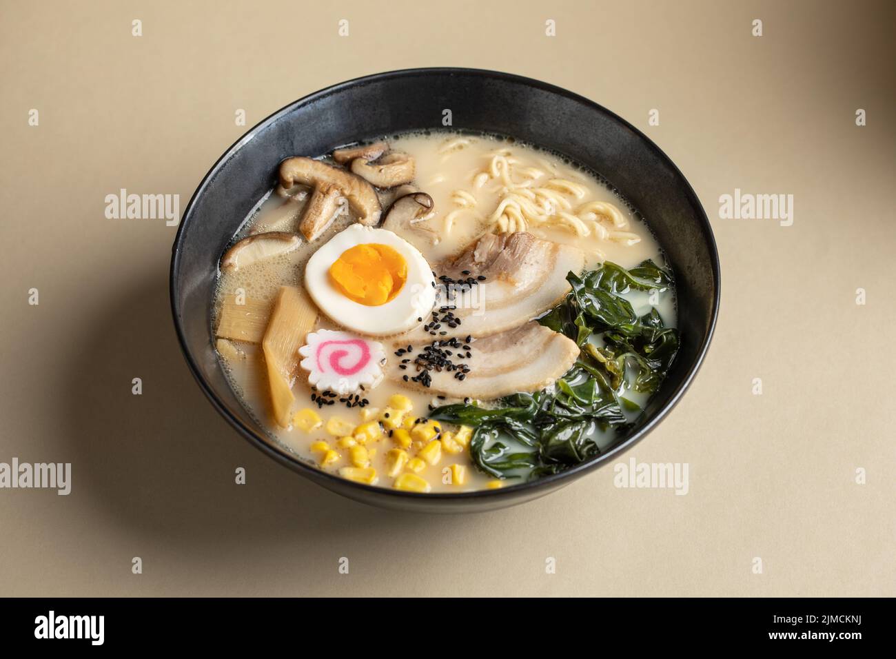 From above of appetizing Japanese ramen with boiled egg and mushrooms served in bowl against beige background Stock Photo