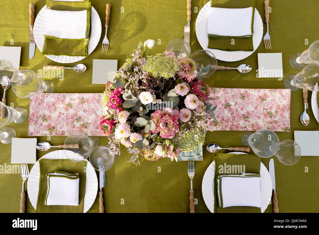 Top view of plates and cutlery served on table with fresh flowers and glassware on terrace during festive event preparation Stock Photo