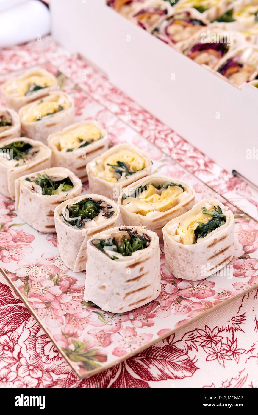 Abundance of tasty tortilla rolls with different fillings served on table with colorful tablecloth near wall during festive event Stock Photo