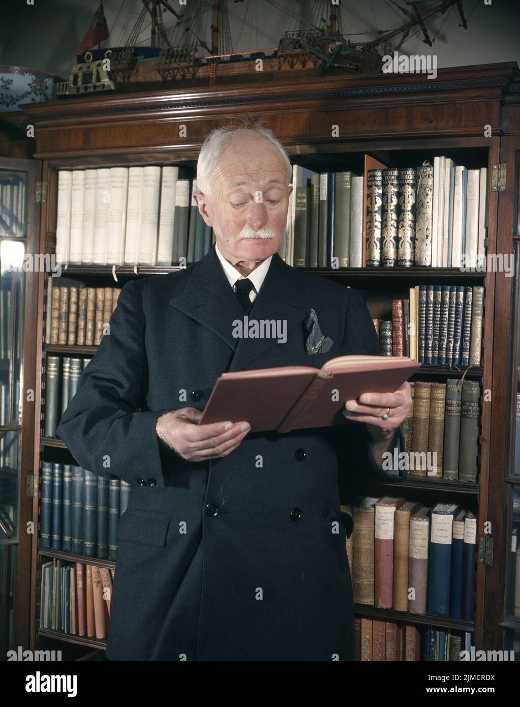 Circa 1965, London, England, United Kingdom: JOHN EDWARD MASEFIELD OM reads a book from his bookcase at home in England. Masefield was an English poet and writer, and Poet Laureate from 1930 until 1967. Among his best known works are the children's novels The Midnight Folk and The Box of Delights, and the poems The Everlasting Mercy and 'Sea-Fever'. (Credit Image: © Keystone USA/ZUMA Press Wire) Stock Photo