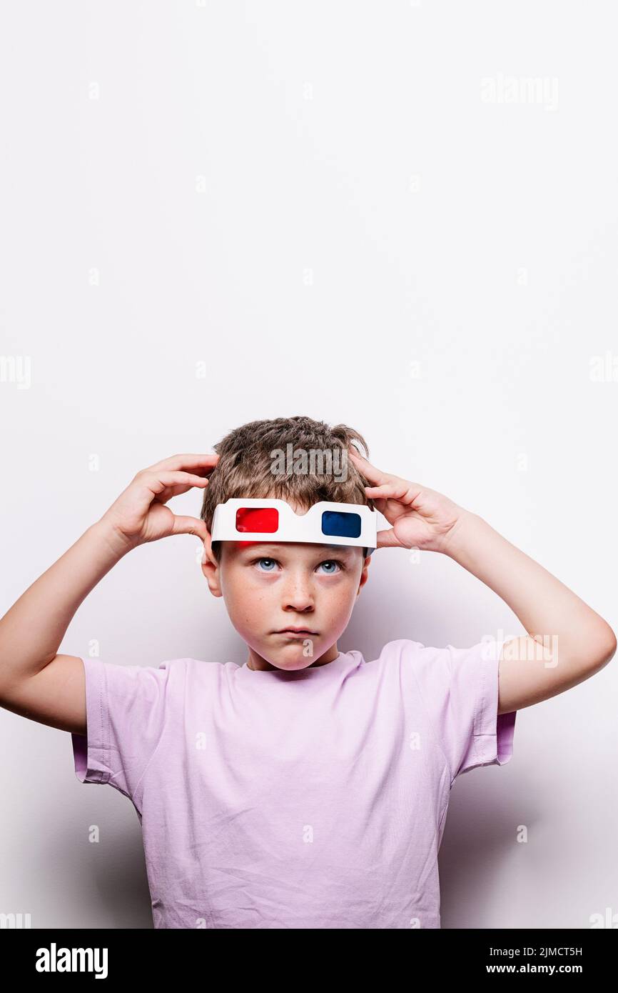 Cute boy in casual wear putting on 3D glasses with colorful lenses