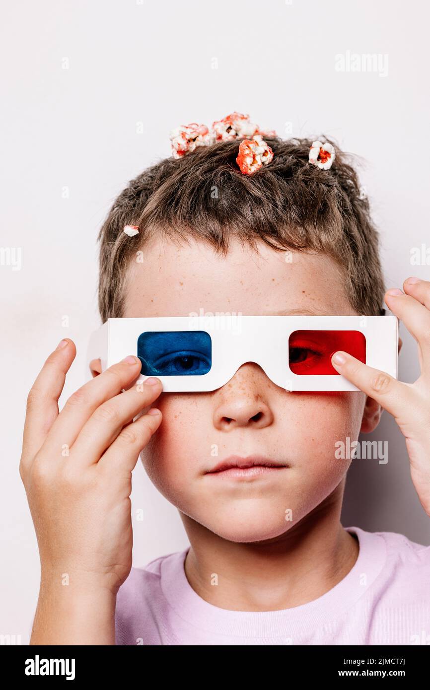 Cute kid in 3D glasses with colorful lenses throwing popcorn over head
