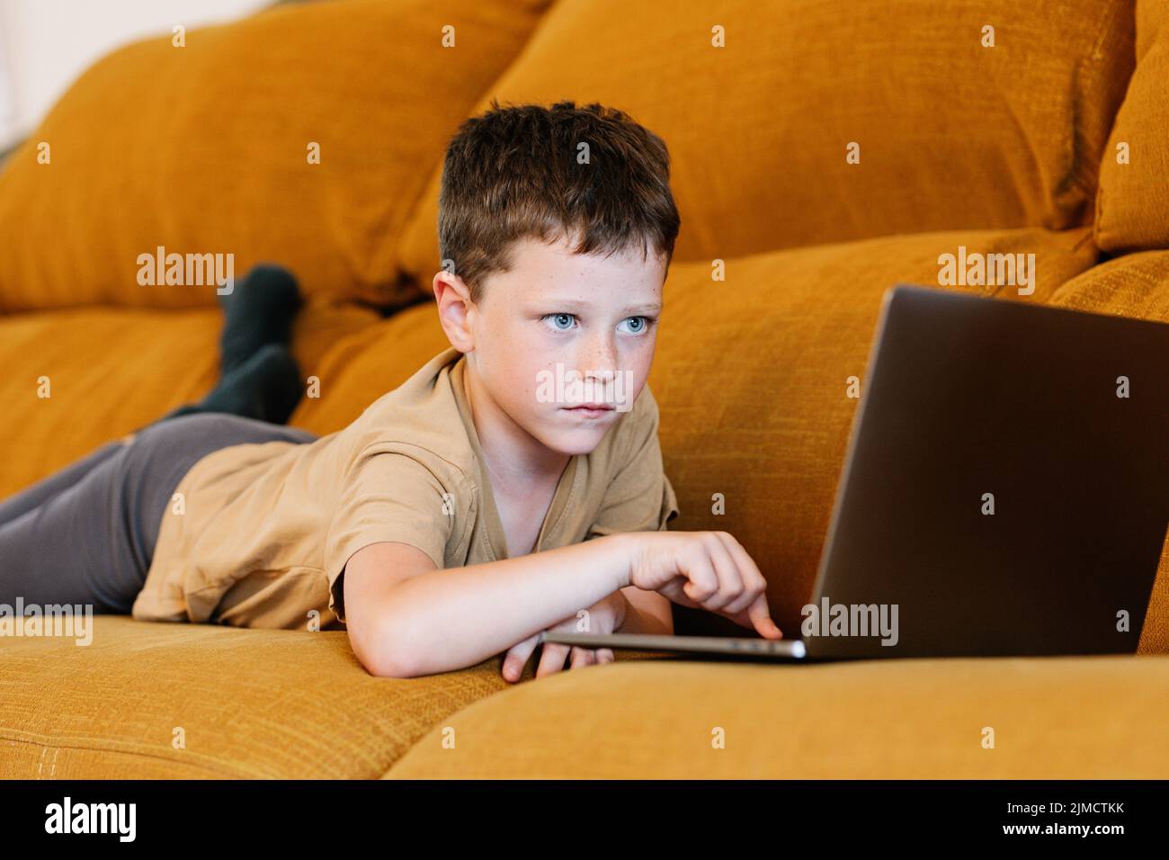 Side view of boy lying on a sofa using the laptop while at home Stock ...