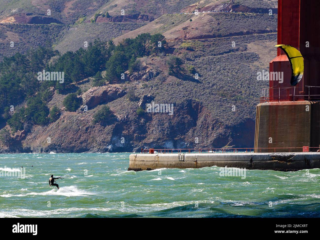 Kitesurfer riding on top whitecaps under the Golden Gate Bridge agains the backdrop of the Marin Headlands Stock Photo