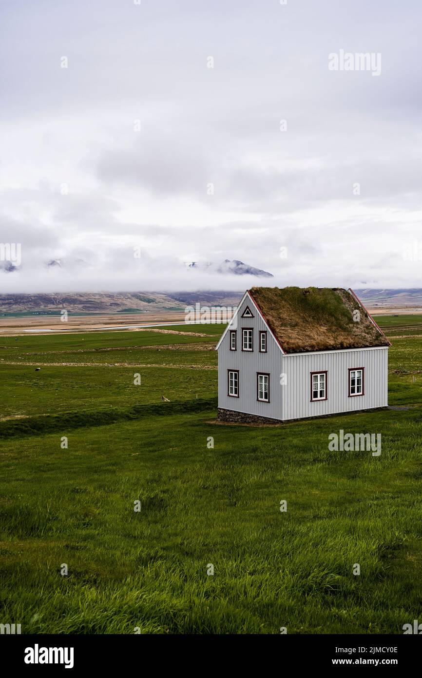 Typical Nordic building with grass roof located on field against cloudy sky in countryside of Iceland in hilly area Stock Photo