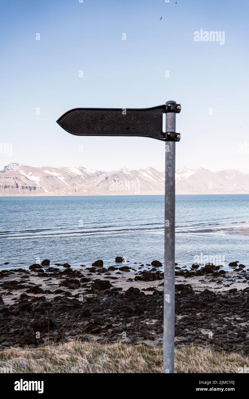 Signpost with pointer located on shore of Westfjords peninsula near rippling sea against mountain ridge in coastal area of Iceland Stock Photo