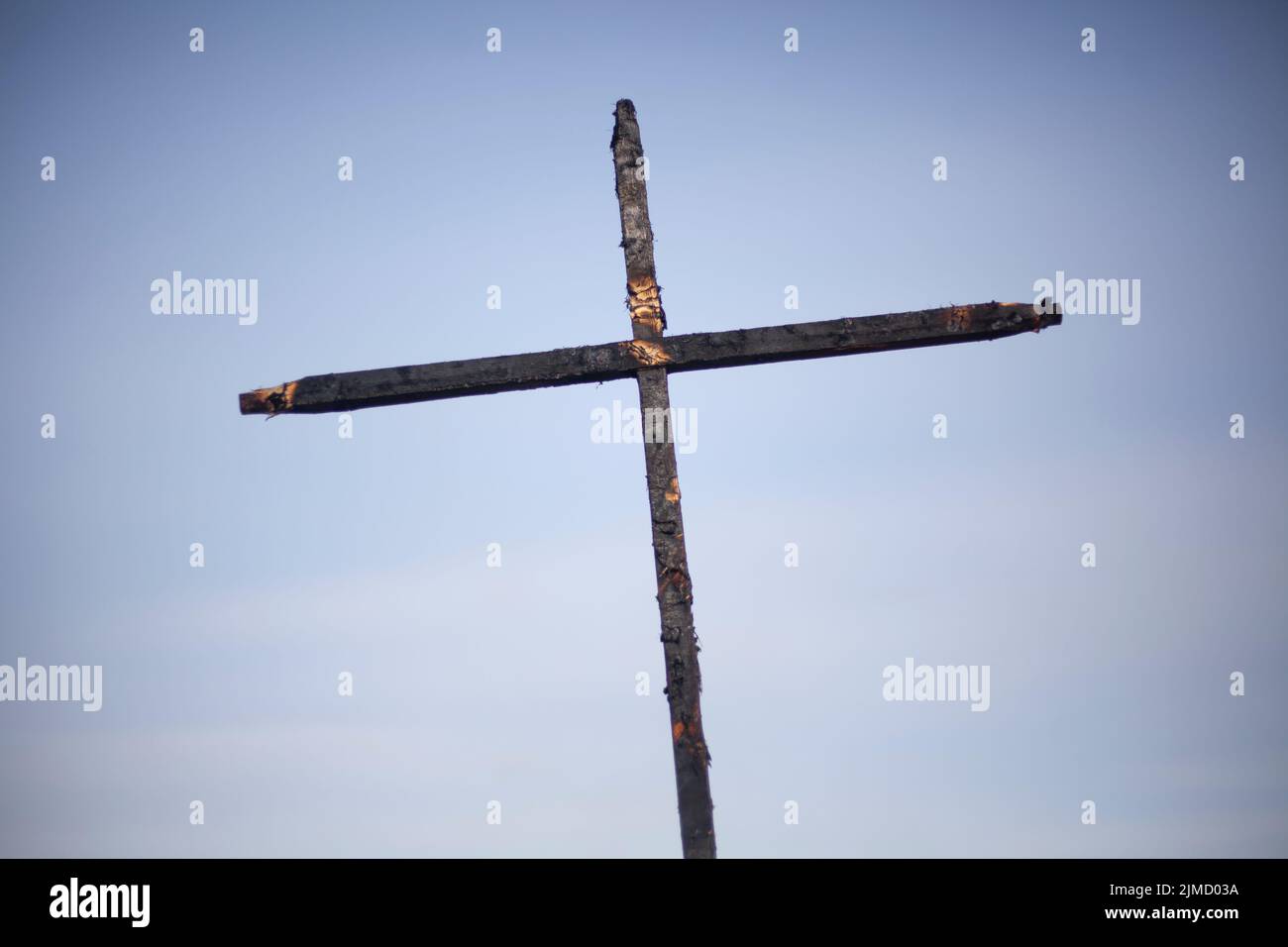 Burnt cross on a blue background. Two daughters covered with coal. Religious symbol. Mystical rite. Sign of Christianity. Stock Photo