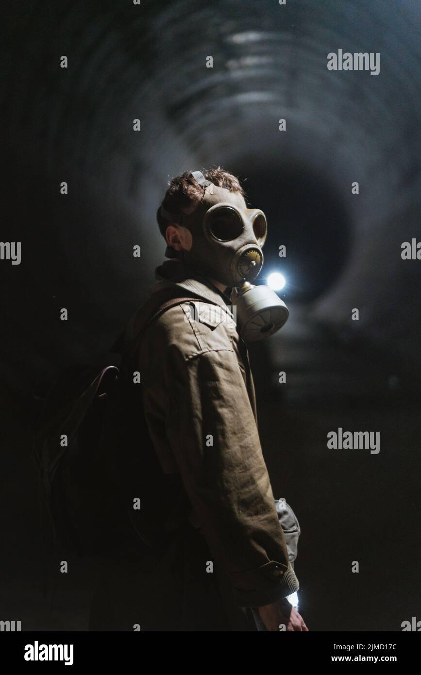 Side view of unrecognizable male explorer in gas mask in dark underground tunnel during apocalypse Stock Photo