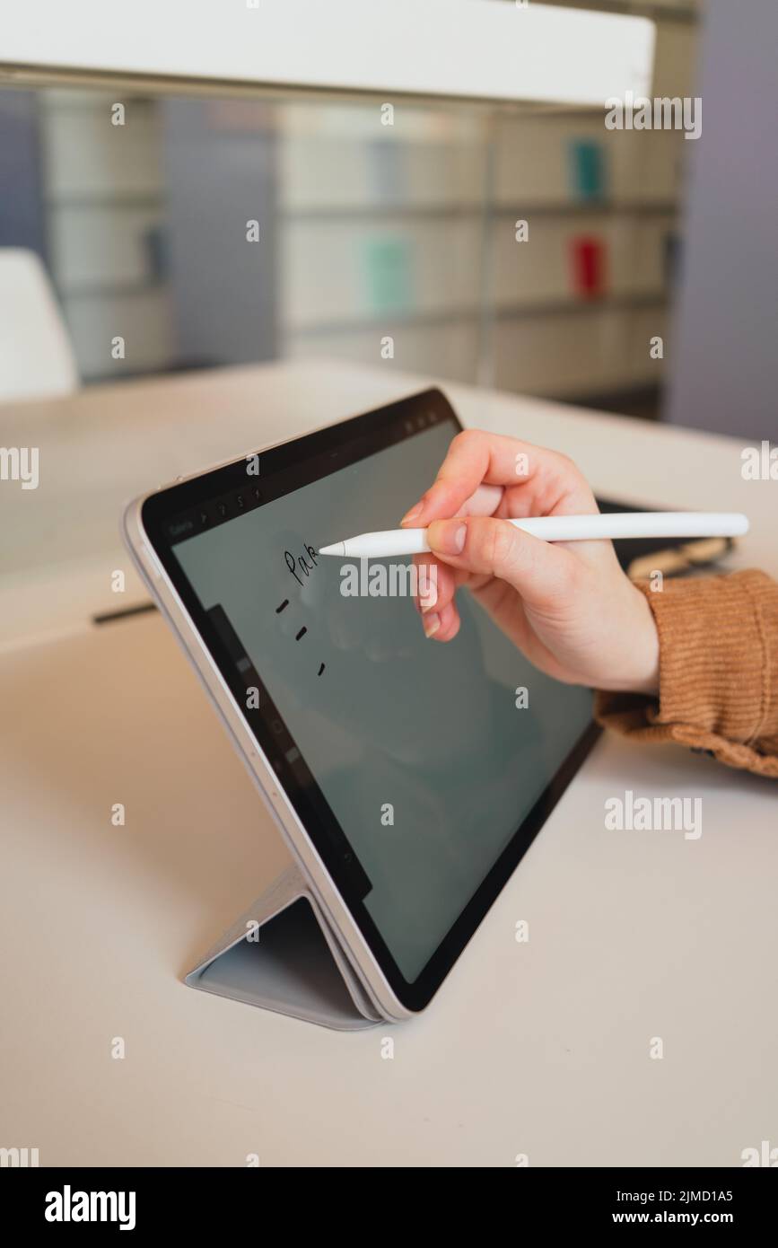 Unrecognizable woman with stylus making notes on tablet while doing homework assignment in library in daytime Stock Photo