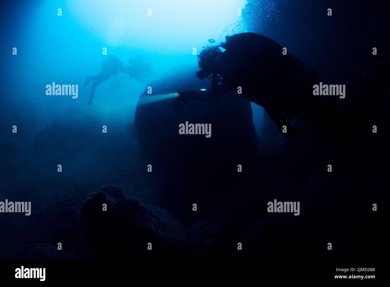 Professional divers with flashlight swimming near old sunken ship covered with moss on bottom of