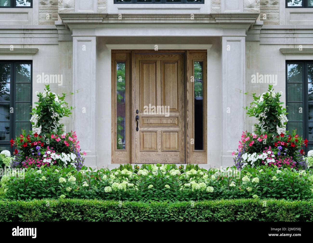 Wood grain front door of house surrounded by columns and summer flowers Stock Photo