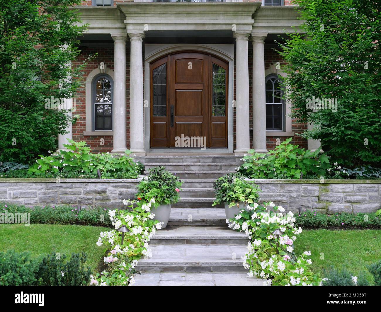 Elegant wood grain front door of house on porch with columns surrounded by shrubbery Stock Photo