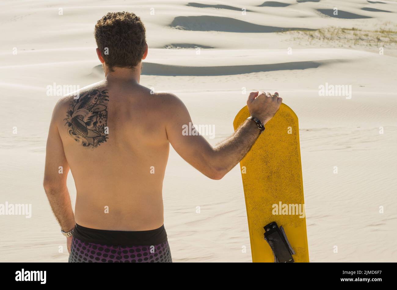 Young man on his back looking at the sand dunes, preparing to practice sandboarding. Stock Photo