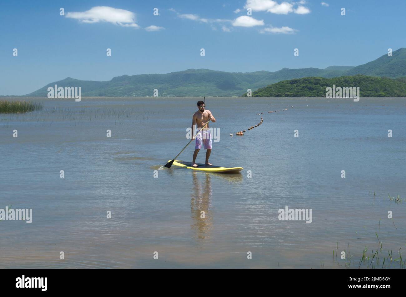 Young man practicing Stand Up Paddle on lake, yellow board, paddling. Paddleboarding. Stock Photo