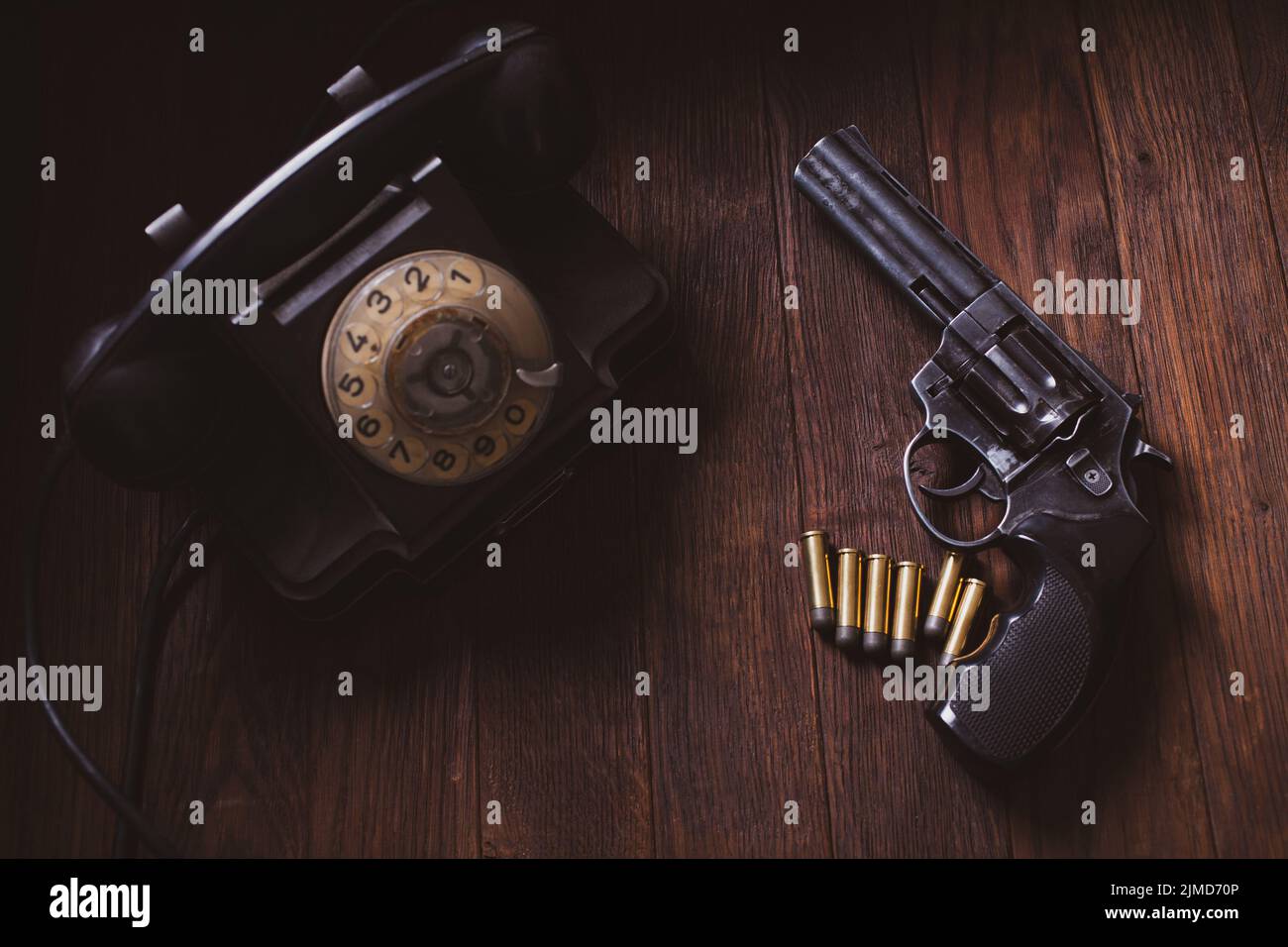 Noir fiction scene - handgun with cartridges and rotary phone on wooden table Stock Photo