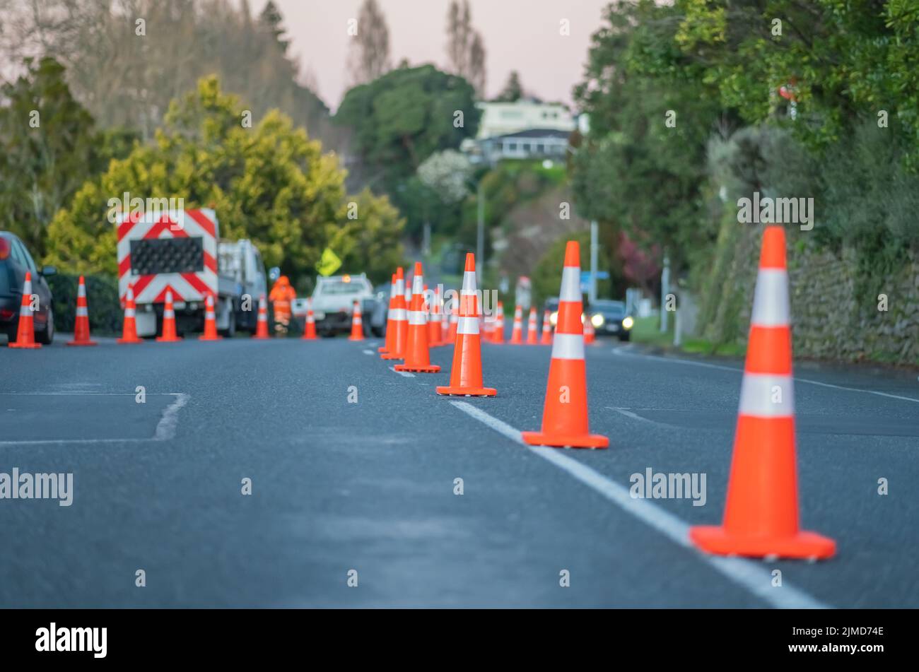 Bright orange road cones reduce street lanes while workers trim edge Stock Photo